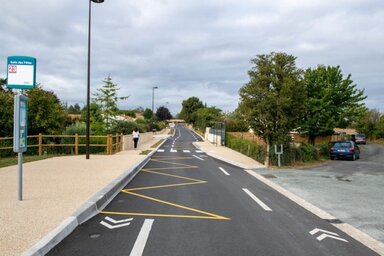 Voie cyclable aménagée avec marquage au sol jaune et blanc, séparée de la chaussée, longeant un arrêt de bus ligne 23