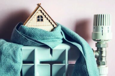 Maquette de maison enveloppée dans un tissu posée sur un radiateur avec tête thermostatique