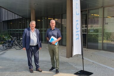 Représentants de Niort Agglo et tanlib posant devant l'entrée du Siège de Niort Agglo, l'un tenant un document de présentation