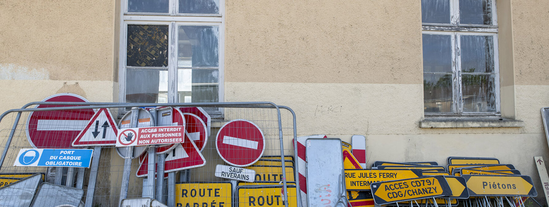 Panneaux 'Route barrée', signaux d'interdiction et barrières de chantier entassés contre la façade d'un bâtiment